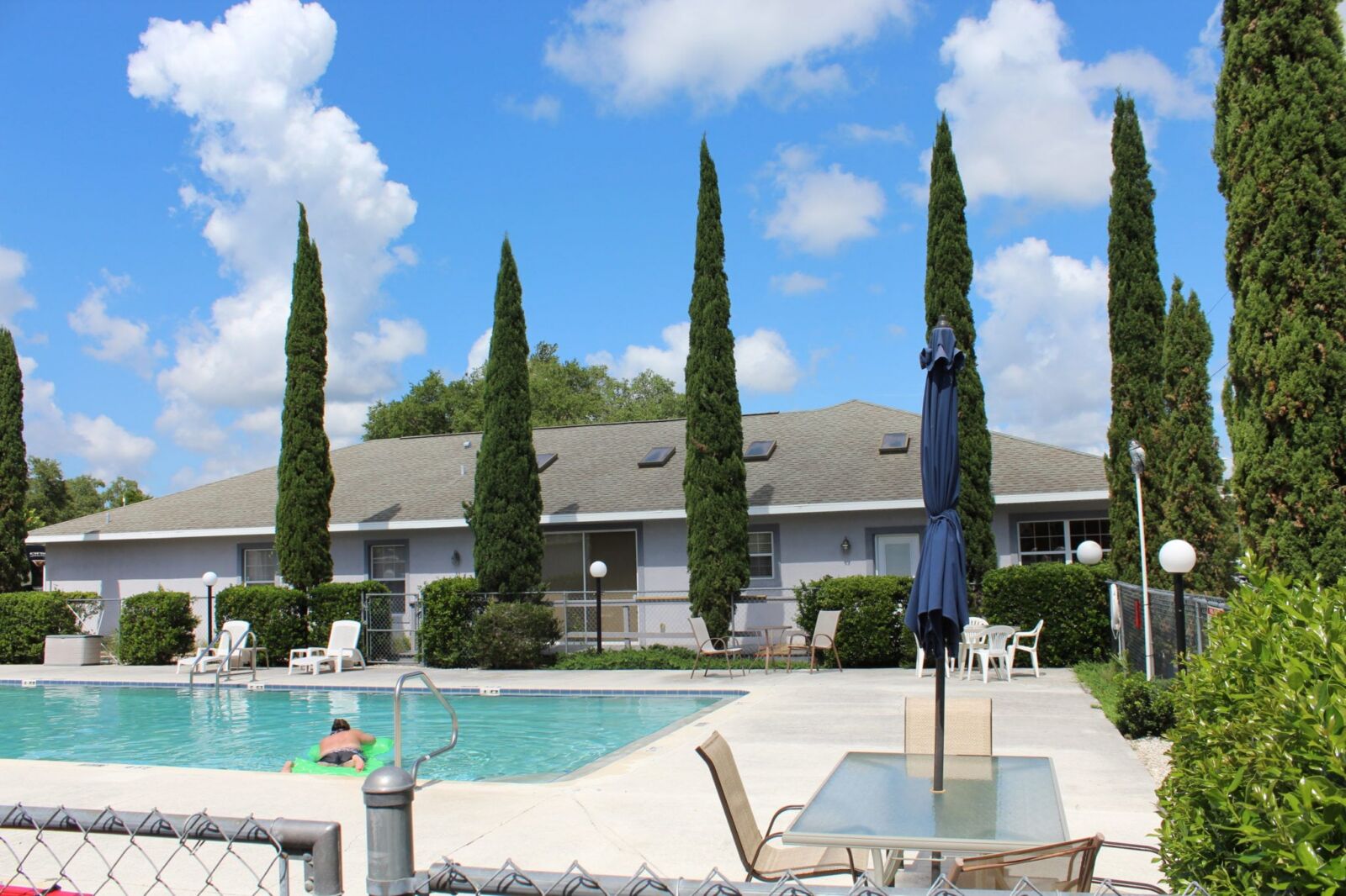 Heated swimming pool and clubhouse framed by tall cypress trees at Quail Roost RV Park